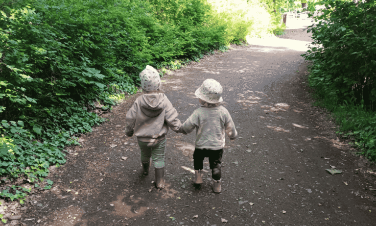Zwei Kinder der Kindertagespflege laufen Hand in Hand einen Waldweg in Leipzig entlang